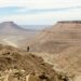 person standing at the edge of a rock mountain facing the mountains during day