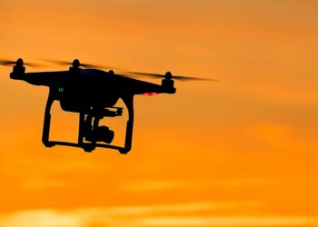 Silhouette of a drone in flight against a orange sunset sky.