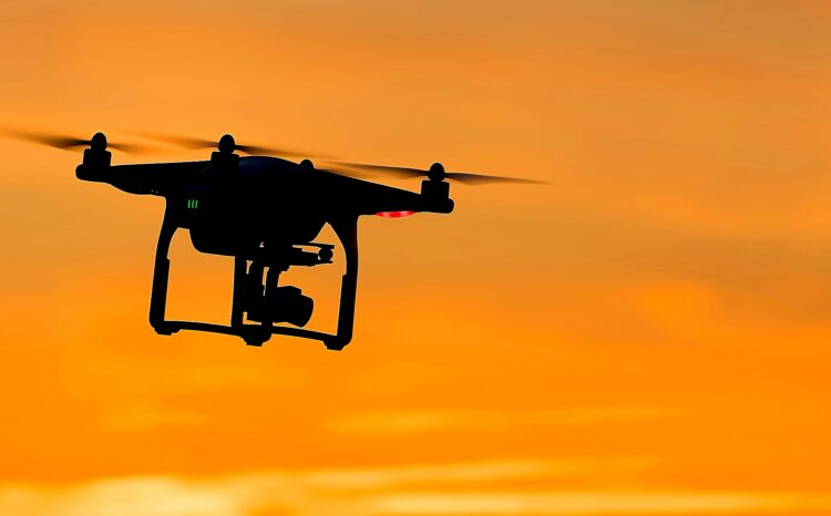 Silhouette of a drone in flight against a orange sunset sky.