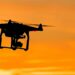 Silhouette of a drone in flight against a orange sunset sky.