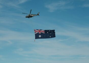 A helicopter flying next to a flag flying in the sky