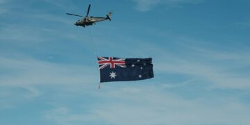 A helicopter flying next to a flag flying in the sky