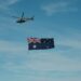 A helicopter flying next to a flag flying in the sky